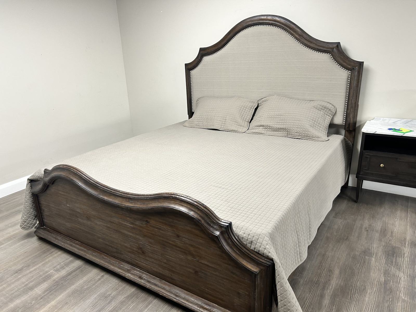 A carved wooden bed frame with an arched headboard and matching nightstand on the showroom floor