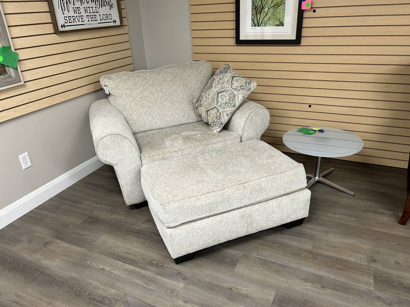 A cream upholstered armchair with matching ottoman and a small round side table