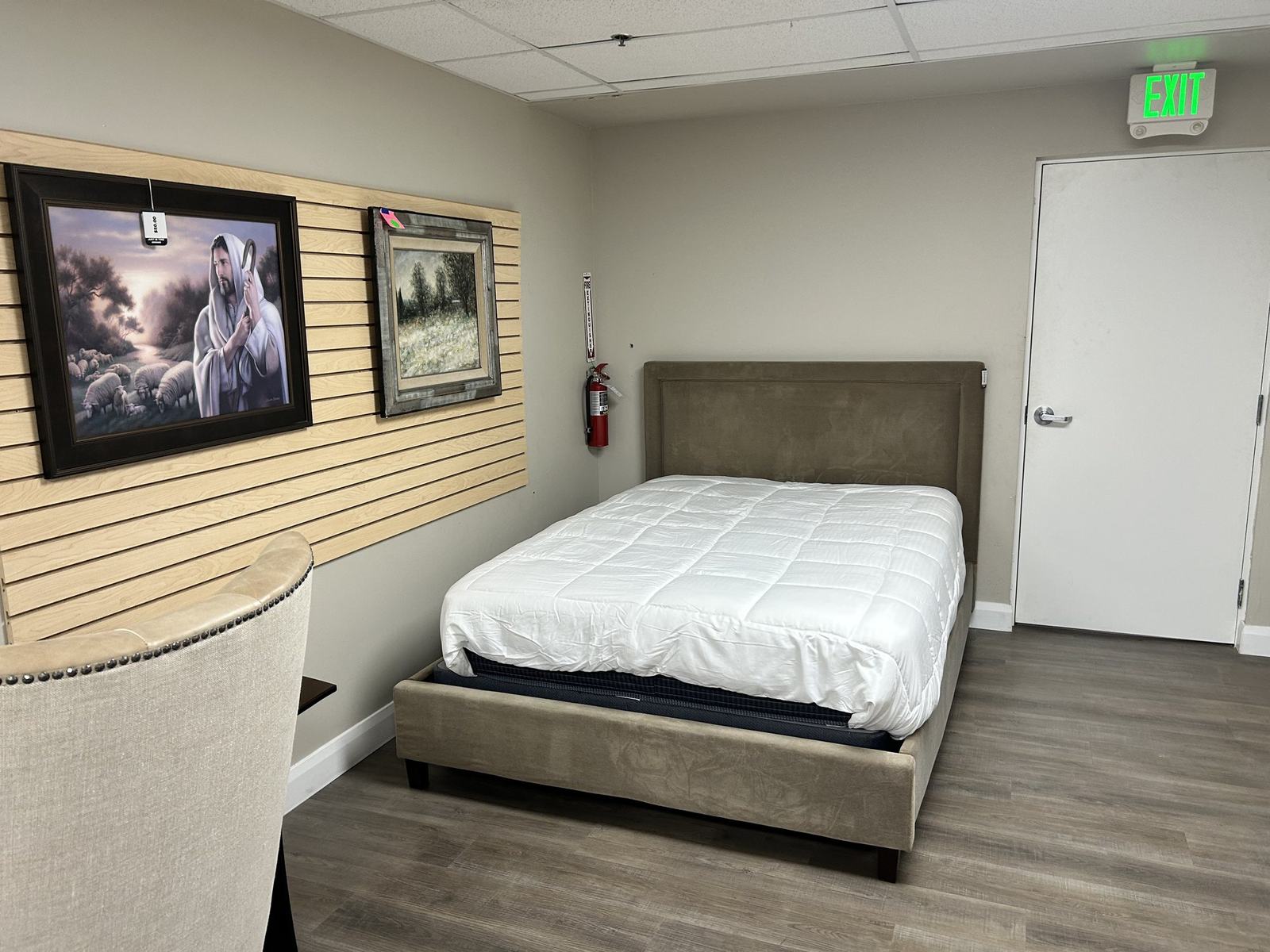 An upholstered platform bed beside framed artwork hung on slatwall in the consignment showroom